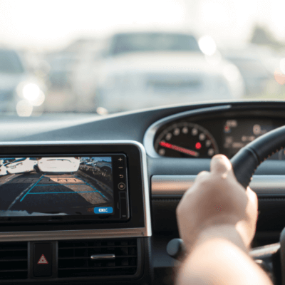 View from the car's back seat of the driver's hand on the steering wheel and a rear area video camera on the dashboard